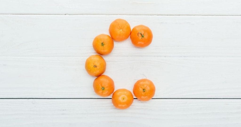 arance formano la lettera C su sfondo di legno a indicare la vitamina C